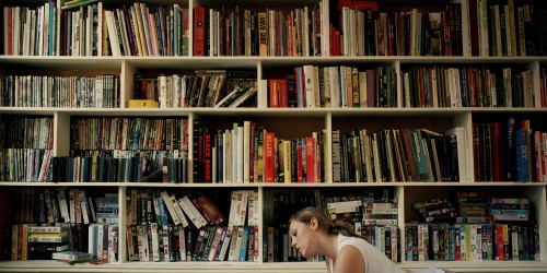 Young woman lying on floor by book shelves, reading, side view